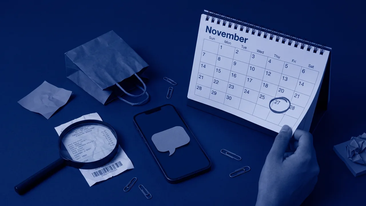 Bodegón en tonos azul marino con un calendario de mesa abierto en noviembre con un día rodeado a bolígrafo, un móvil con un bocadillo de conversación recortado en papel, una bolsa de compra pequeña y una lupa sobre un tique arrugado, metáfora del consumidor que investiga con IA semanas antes del Black Friday