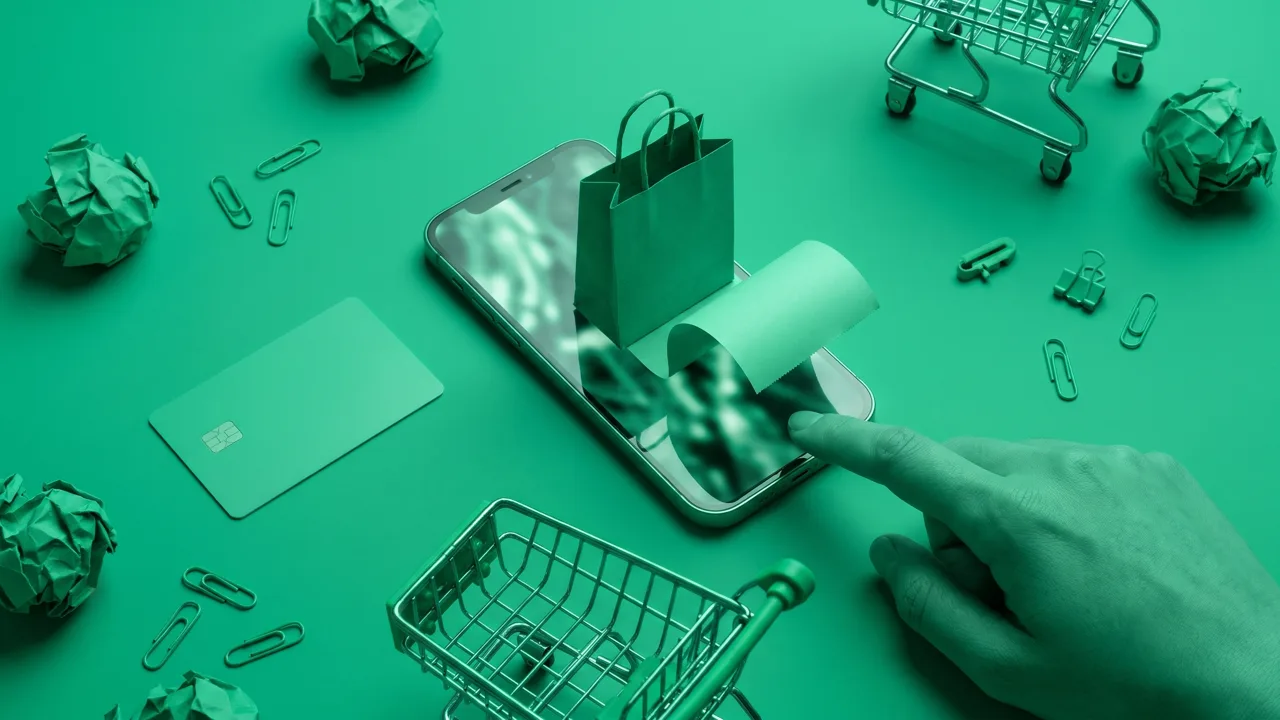 Bodegón cenital en tonos verde esmeralda con un smartphone cuyo feed vertical expulsa una bolsa de la compra y un ticket sobre la mesa, una tarjeta de crédito, un carrito en miniatura, bolas de papel arrugado y una mano que va a pulsar la pantalla, metáfora del checkout que ahora vive dentro del feed de TikTok